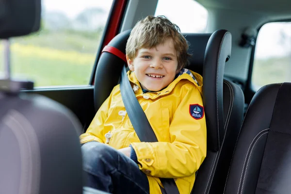 Adorabile carino bambino in età prescolare seduto in auto in cappotto giallo pioggia . — Foto Stock