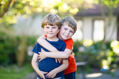 Çocuklar, İkizler ve yaz gününde sarılma kardeşler iki küçük etkin okul çocuklar