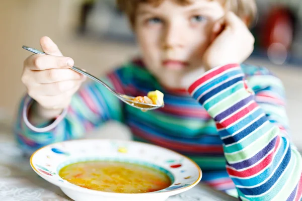 Entzückender kleiner Schuljunge isst Gemüsesuppe drinnen. — Stockfoto