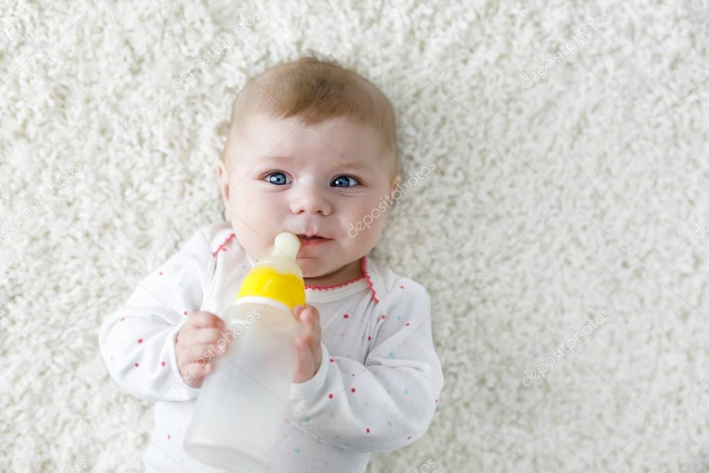 Cute adorable ewborn baby girl holding nursing bottle and drinking formula milk