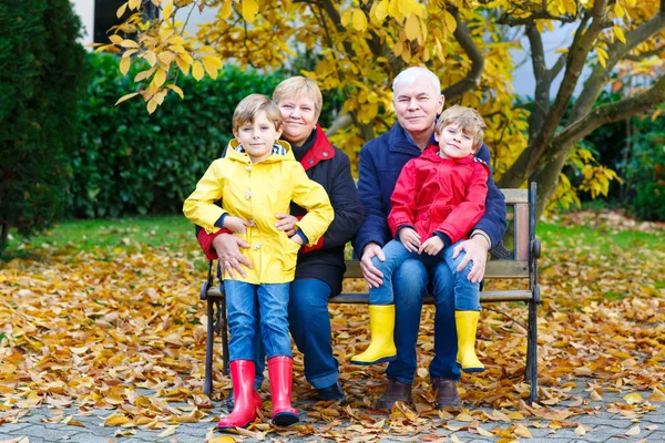 Dziadek, Babcia i dwóch małych chłopców dzieci, wnuki, siedząc w jesienny park. — Zdjęcie stockowe