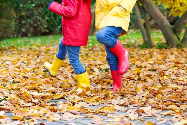 Двоє маленьких дітей грають у червоно-жовтих гумових черевиках в осінньому парку — стокове фото