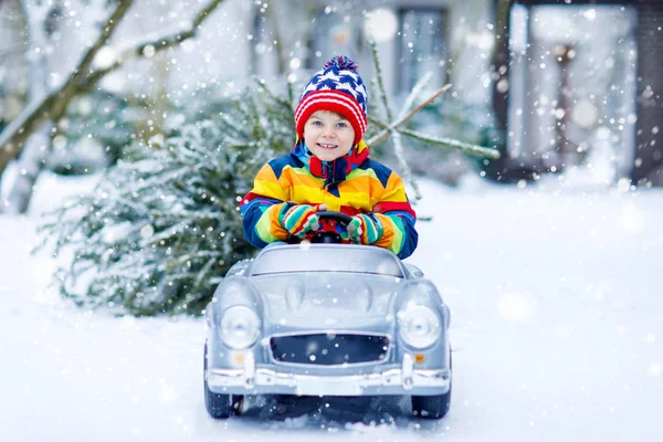 Grappig klein lachend kind jongen rijden speelgoed auto met kerstboom. — Stockfoto