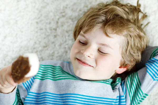 Little blond kid boy with curly hairs eating ice cream popsicle with chocolate at home — Stock Photo, Image