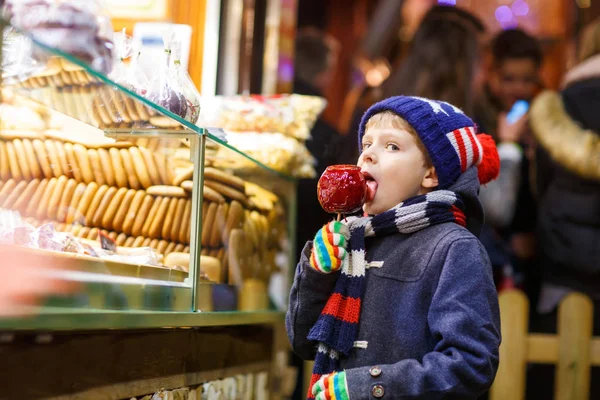 Niño pequeño comiendo azúcar manzana dulces de pie en el mercado de Navidad —  Fotos de Stock