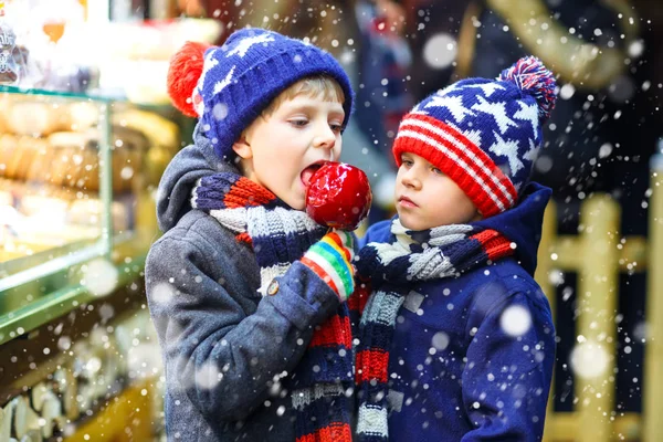 2 小さな子供男の子砂糖のリンゴのお菓子を食べてクリスマス マーケットの上に立つ — ストック写真