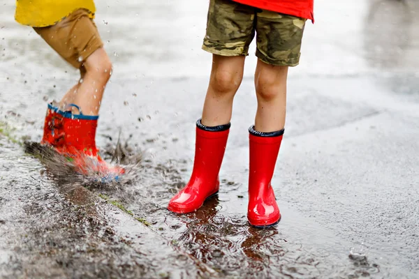 Dos niños con botas de lluvia rojas saltando en un charco . — Foto de Stock