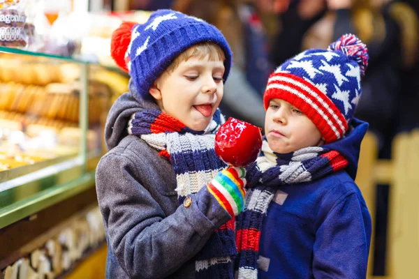 2 小さな子供男の子砂糖のリンゴのお菓子を食べてクリスマス マーケットの上に立つ — ストック写真