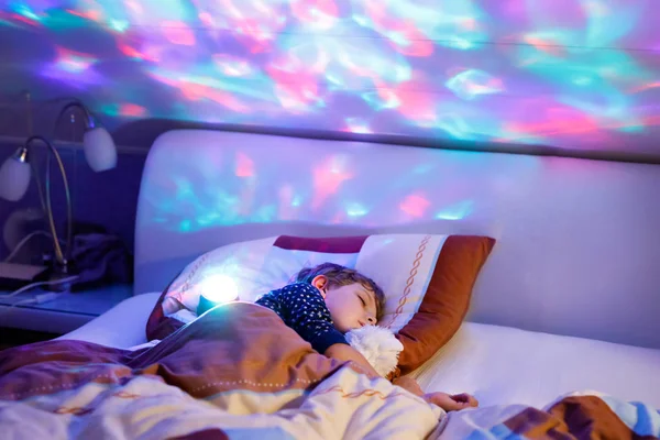 Pequeno menino pré-escolar dormindo na cama com lâmpada colorida . — Fotografia de Stock