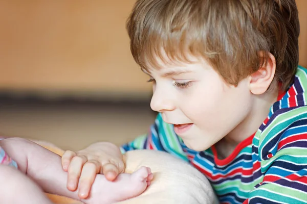 Niño pequeño besándose y jugando con el pie del bebé recién nacido . — Foto de Stock