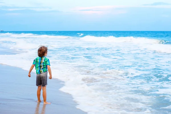 Kleine jongen jongen op zoek op zonsondergang op het strand van de Oceaan — Stockfoto