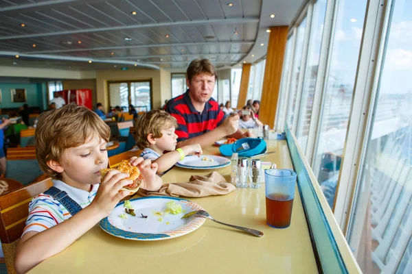 Two preschool kids boys and father eating hamburger sitting in cafe on cruise ship