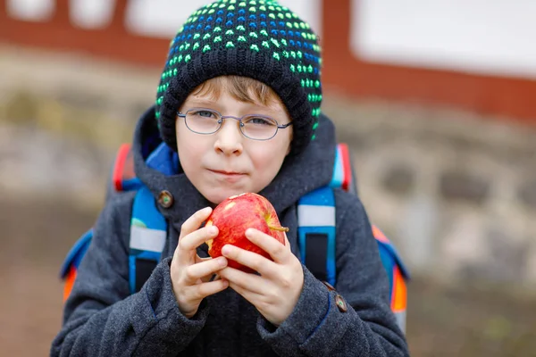 Niño pequeño con anteojos caminando desde la escuela y comiendo manzana —  Fotos de Stock