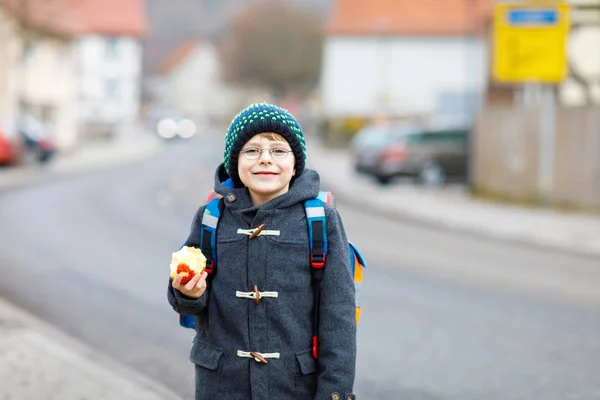 Niño pequeño con anteojos caminando desde la escuela y comiendo manzana — Foto de Stock