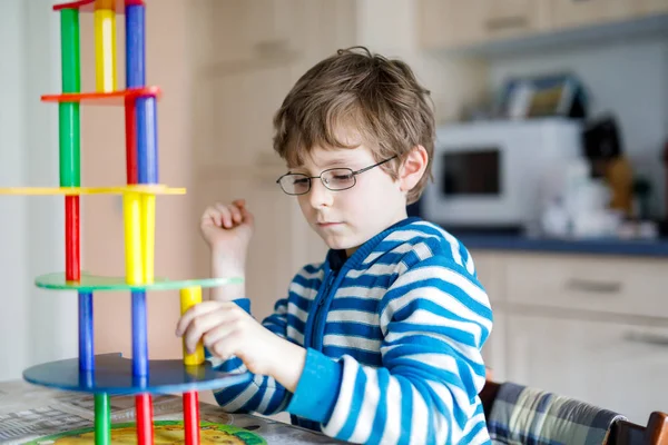 Мальчик в очках играет с большим количеством красочных деревянных блоков игры в помещении — стоковое фото