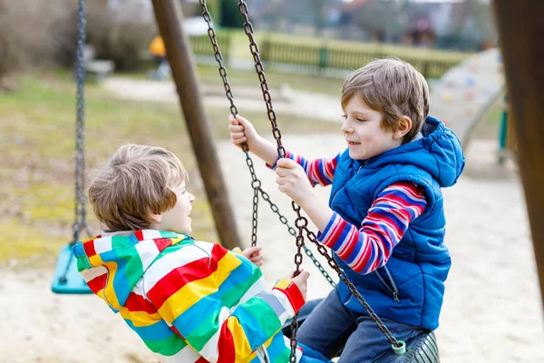 Two little kid boys having fun with chain swing on outdoor playground — Stock Photo, Image