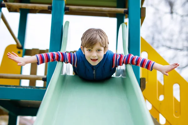 Felice ragazzo biondo che si diverte e scivola sul parco giochi all'aperto — Foto Stock