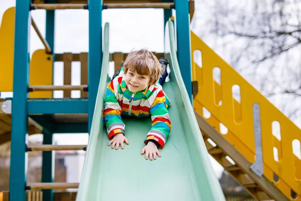 Felice ragazzo biondo che si diverte e scivola sul parco giochi all'aperto — Foto Stock