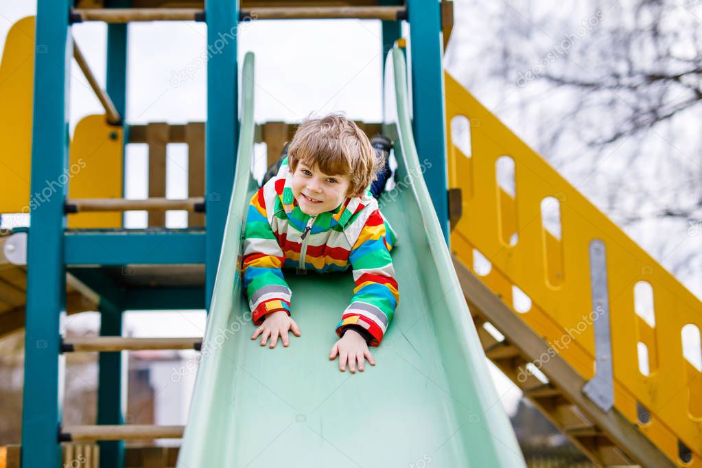 Happy blond kid boy having fun and sliding on outdoor playground