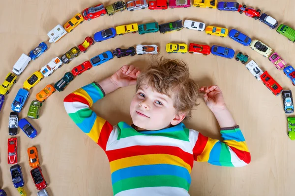 Söt liten blond kid pojke leker med massor av leksaksbilar inomhus. — Stockfoto