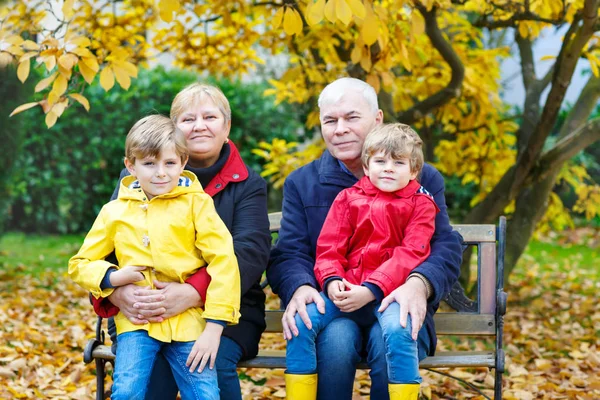 Dědeček, Babička a dva malé dítě chlapce, vnoučata sedí v podzimním parku. — Stock fotografie