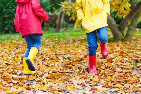 Dwa małe dzieci bawiące się w czerwone i żółte kalosze w jesienny park — Zdjęcie stockowe