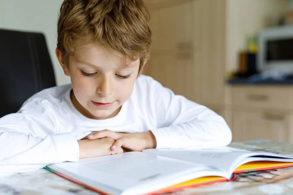 Piccolo ragazzo della scuola bionda con gli occhiali che legge un libro a casa — Foto Stock