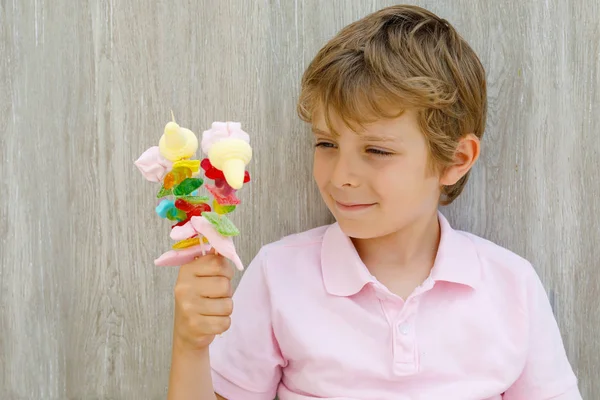 Happy little kid boy holding marshmallow skewer in hand. Child with different unhelthy colorful sweets — Stock Photo, Image