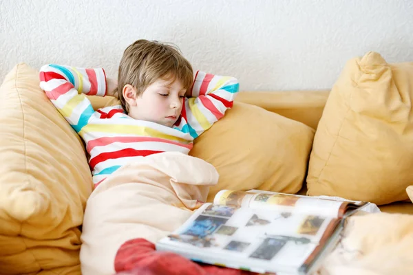 Маленький блондин-школьник в очках читает книгу дома — стоковое фото