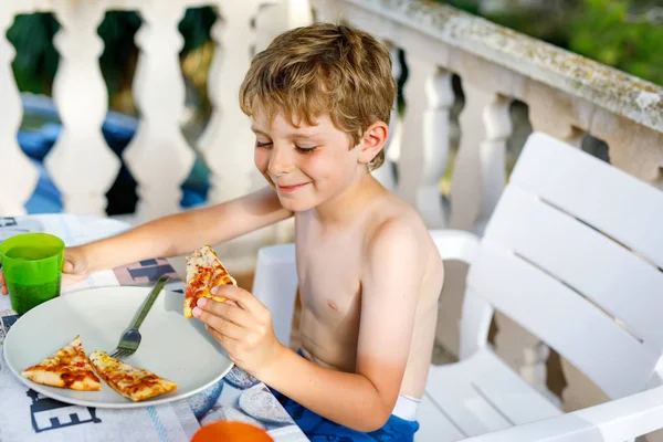 Cute healthy preschool kid boy eats fresh pizza sitting on terrace in summer, outdoors — Stock Photo, Image