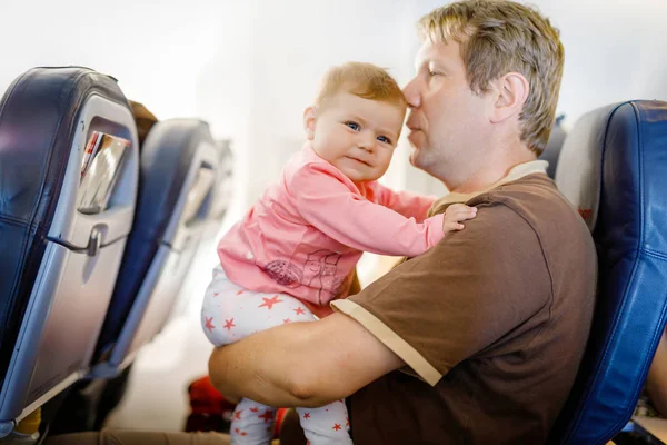 Молодой уставший отец и его плачущая маленькая дочь во время полета на самолете собирается в отпуск — стоковое фото