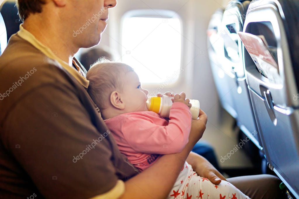 Father holding his baby daughter during flight on airplane going on vacations