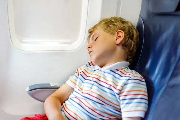 Niño durmiendo durante un largo vuelo en avión. Niño sentado dentro de la aeronave por una ventana — Foto de Stock