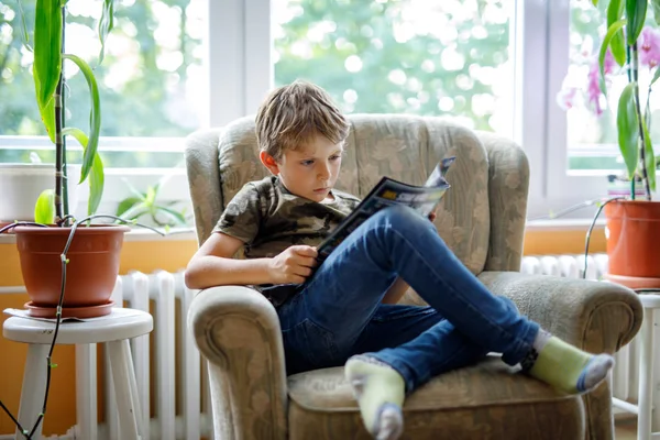 Ragazzo biondo carino che legge rivista in camera domestica . — Foto Stock