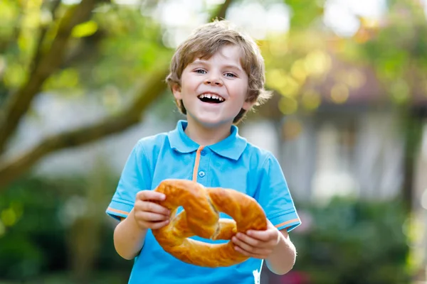 Adorável menino pequeno comendo enorme grande bávaro alemão pretzel. — Fotografia de Stock