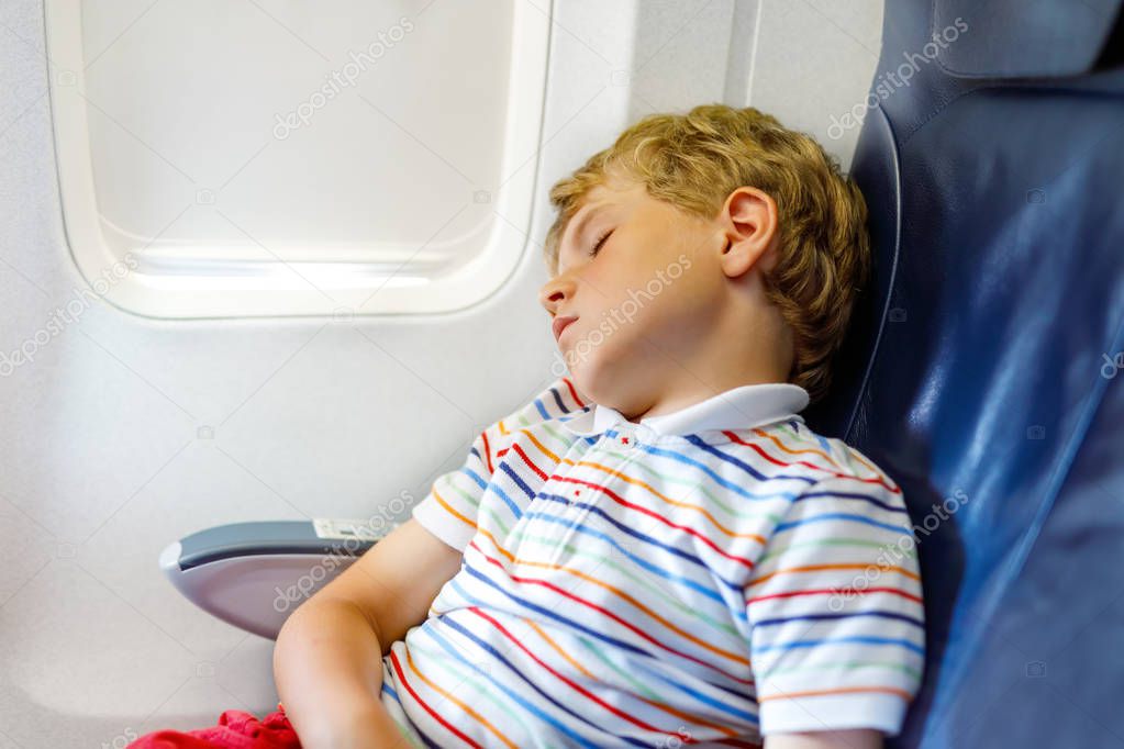 Little kid boy sleeping during long flight on airplane. Child sitting inside aircraft by a window