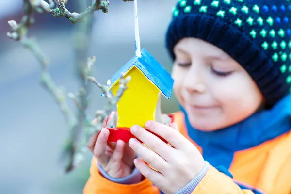 Little kid hanging bird house on tree for feeding in winter — Stock Photo, Image