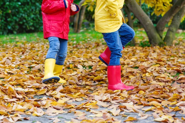 Primo piano delle gambe dei bambini in stivali di gomma che ballano e camminano attraverso le foglie autunnali — Foto Stock