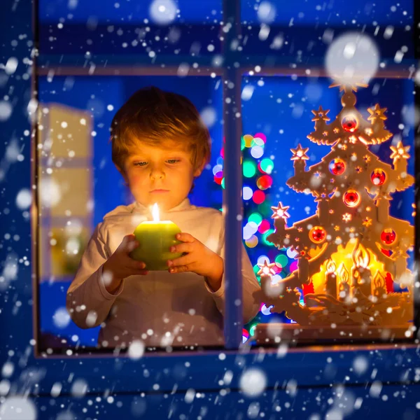 Kleiner Junge steht zur Weihnachtszeit am Fenster und hält — Stockfoto