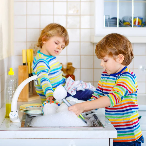 Dos niños pequeños lavando platos en la cocina doméstica — Foto de Stock