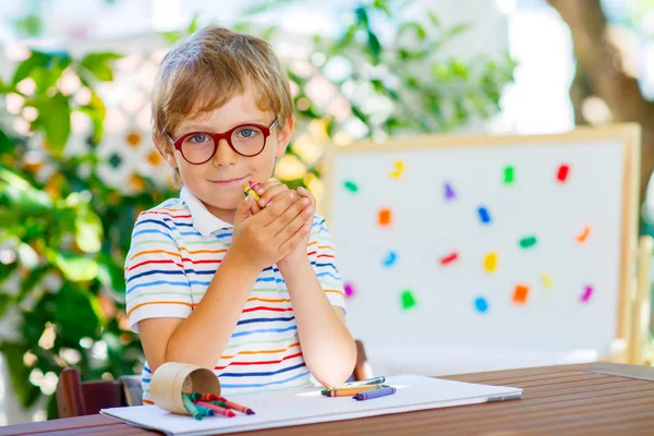 Маленький школьник в очках держит восковые карандаши — стоковое фото