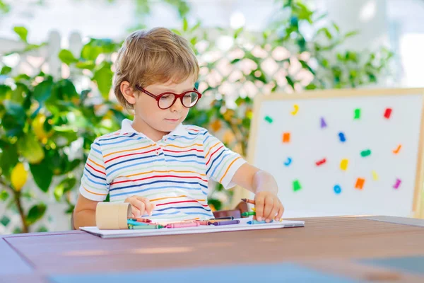 Mały chłopiec dziecko szkoły w okularach gospodarstwa kredki woskowe — Zdjęcie stockowe