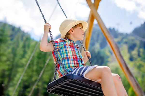 Legrační kluk baví s řetězci swing na venkovním hřišti na slunečný den — Stock fotografie