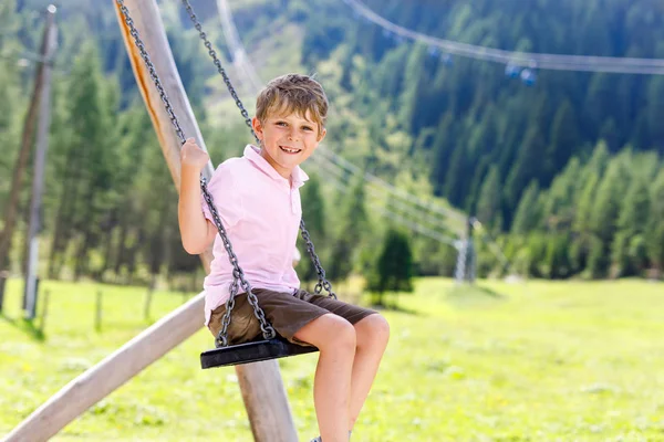 Funny kid boy having fun with chain swing on outdoor playground on sunny day — Stock Photo, Image