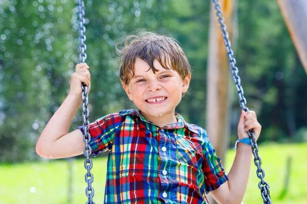 Vicces gyerek fiú szórakozik a swing-lánc a szabadtéri játszótéren eső alatt — Stock Fotó