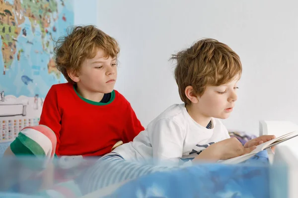 Dos niños pequeños en pijama leyendo un libro en la cama . — Foto de Stock