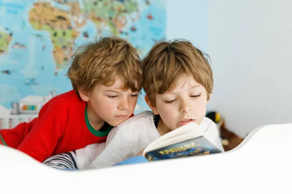 İki küçük çocuk pijama yatakta kitap okurken erkek. — Stok fotoğraf