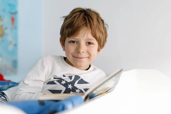 Cute blond little kid boy in pajamas reading book in his bedroom — Stock Photo, Image