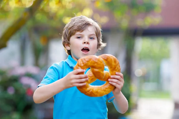 Schattige kleine jongen eten enorme grote bavarian duits pretzel. — Stockfoto