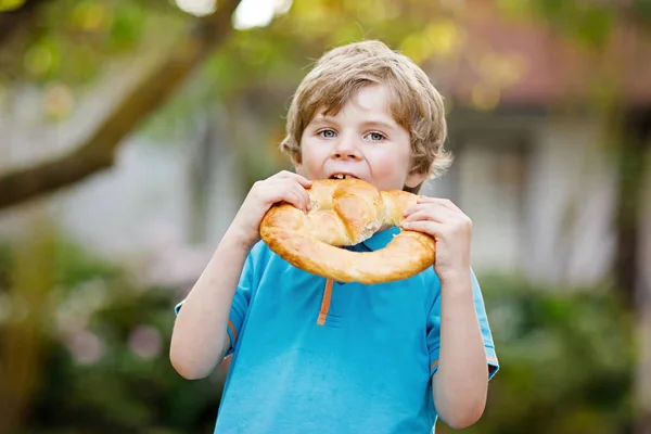 Uroczy mały chłopiec jedzący wielkiego bawarskiego niemieckiego precla. — Zdjęcie stockowe
